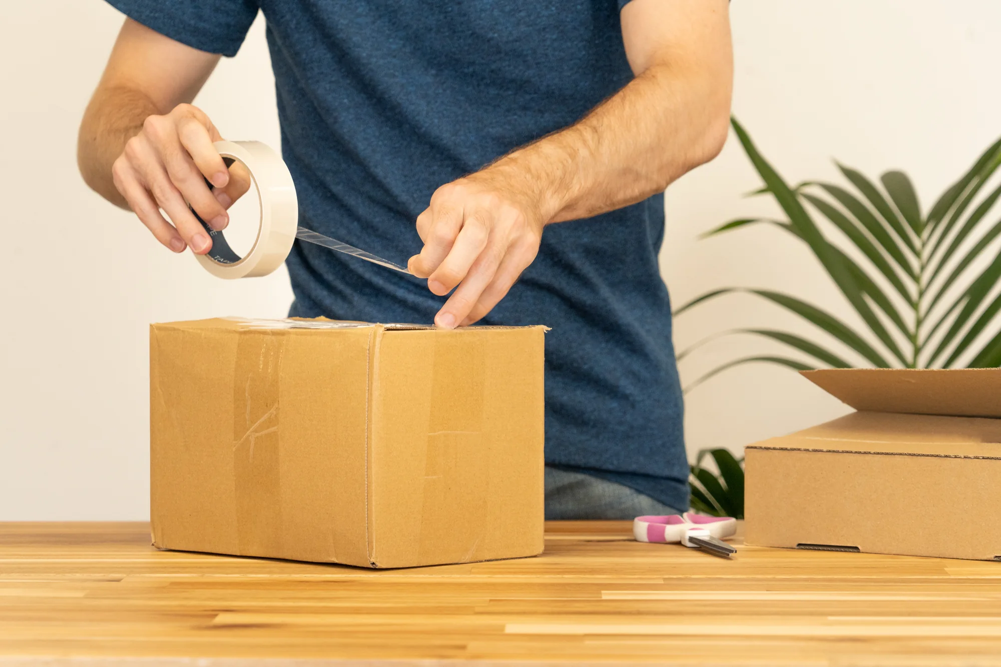 Hands applying packing tape to a cardboard carton